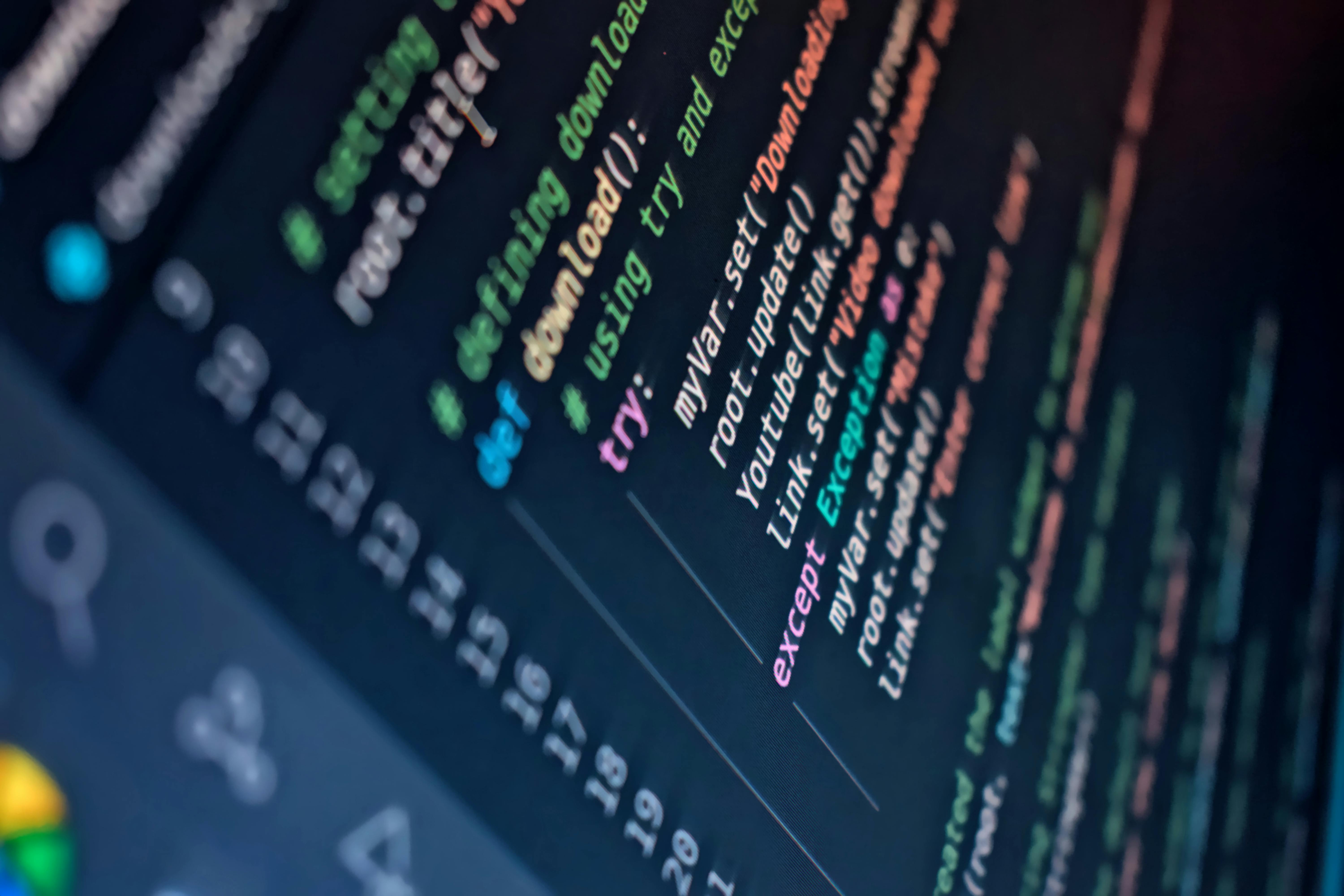 Close-up van computerscherm met kleurrijke programmeercode. De code is scherp in beeld, met verschillende programmeerconcepten zichtbaar zoals 'defining', 'download', 'try', en 'except'. Deze afbeelding illustreert het complexe en gedetailleerde werk van softwareontwikkeling, waarbij nauwkeurigheid en technische expertise cruciaal zijn.